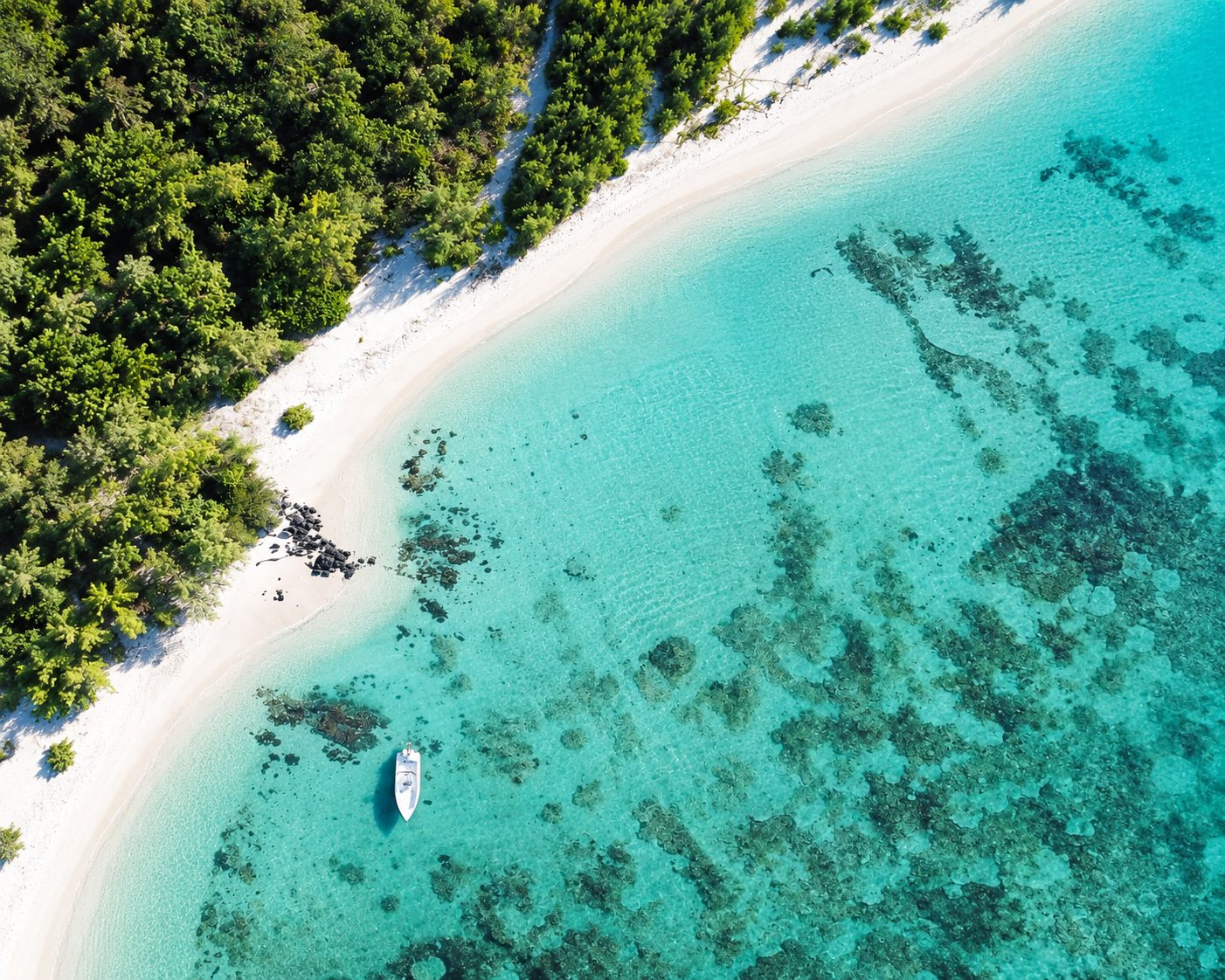 Aerial view of a white-sand beach and turquoise lagoon in Mauritius, with a boat anchored offshore